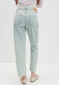 Hellblaue Denim-Jeans mit geradem Bein, sichtbaren Gesäßtaschen und einem braunen Lederpatch über dem Bund. Weiche Textur.