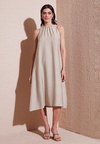 A sleeveless, knee-length beige dress with a gathered neckline made of lightweight fabric, featuring a loose fit and subtle texture.