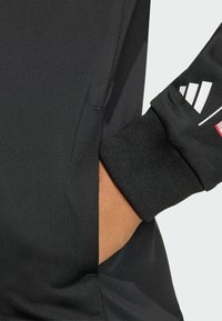 Musta urheilupaita, jossa on istuva muotoilu, teksturoitu kangas, peukaloreiät hihansuiden kohdalla ja piilotettu sivutasku.