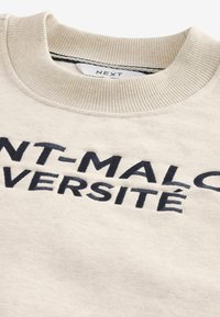 Cremefarvet sweatshirt med ribbet halsudskæring, prydet med marineblå broderet tekst, der står "SAINT-MALO UNIVERSITÉ." Blødt stof.