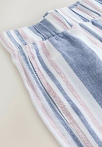 Gestreifter Stoff mit weißen, blauen und roten Linien, mit strukturierter Oberfläche und elastischem Bund. Fokus auf das Detail des zerknitterten Stoffs.