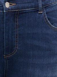 Σκούρο μπλε τζιν με ορατό κίτρινο ράψιμο, μεταλλικό κουμπί και μπροστινή τσέπη στη δεξιά πλευρά.