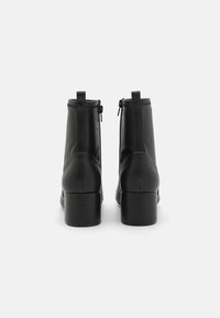 Bottines en cuir noir avec un design épuré, des orteils ronds et des talons carrés ; comportent une fermeture éclair et un minimum de détails de couture.