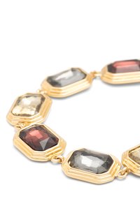 Pulsera de oro con grandes gemas facetadas en forma octogonal en tonos rojo oscuro, gris y beige claro, unidas en un círculo.