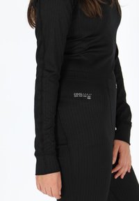 Sort atletisk outfit bestående af en langærmet top og bukser med lodret ribbet tekstur. Materialet mærket som COOLMAX® til fugtstyring.