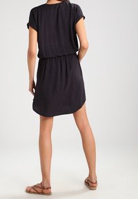 Vestido negro de manga corta y corte holgado, con cintura elástica y dobladillo redondeado. La tela ligera presenta un patrón sutil.