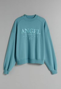 Teal sweatshirt med rund halsringning, raglanärmar och ribbade muddvästar. Har vit upphöjd text: "ANGEL ENERGY JUST FEEL IT" över framsidan.