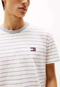 Stribet kortærmet t-shirt i lyserød og grå bomuld. Har en rund hals og et lille logo patch i blå, rød og hvid med teksten "TOMMY JEANS".