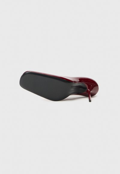 Pantof burgundy cu toc înalt, cu un finisaj lucios din piele patent, vârf ascuțit și talpă neagră. Toc subțire stiletto și textură netedă.