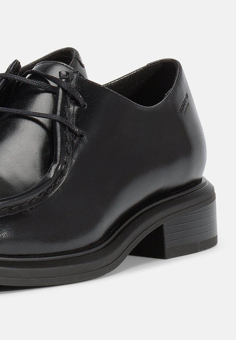 Zapato oxford de cuero negro con punta redonda, cordones y pequeño tacón cuadrado. Textura suave y sutil detalle de costura en la parte superior.