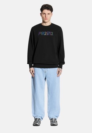Czarny sweatshirt z napisem "PROSTO." w kolorze gradientowym na klatce piersiowej, w połączeniu z jasnoniebieskimi, luźnymi dżinsami i szarymi trampkami.