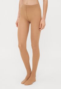 Collants couleur chair avec une texture lisse et légère, dotés d'une taille haute et d'un design ajusté, couvrant complètement les jambes.