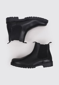 Botas Chelsea de cuero negro con paneles laterales elásticos, suela de goma y banda de rodadura texturizada para un buen agarre. Diseño minimalista con tiradores.