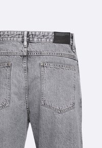 Graue Denim-Jeans mit geradem Schnitt, zwei Gesäßtaschen und einem schwarzen Lederlabel am Bund. Strukturierter Stoff mit ausgewaschenem Finish.
