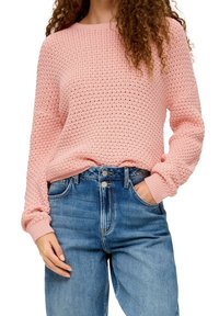 Pull en tricot rose clair avec un motif texturé, manches longues et poignets côtelés. Associé à un jean en denim bleu taille haute.