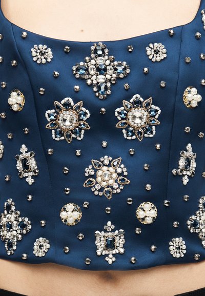 Σκούρο μπλε σατέν ένδυμα διακοσμημένο με διάφορα σχέδια από μαργαριτάρια, κρύσταλλα και σκούρες μπλε πολύτιμες πέτρες σε μορφή λουλουδιών και γεωμετρικών μοτίβων.