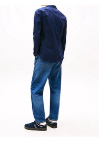 Camicia a bottoni blu navy, jeans blu larghi e sneakers navy con accenti grigi. Design semplice, texture liscia, vestibilità casual.