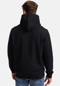 Un sweat à capuche noir avec un motif texturé, doté d'une capuche et de poignets côtelés, associé à un jean bleu. Le tissu semble doux et chaud.