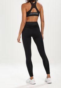 Brasile sportivo nero con design a schiena scoperta e pannello in rete, abbinato a leggings neri a vita alta con cuciture eleganti e una superficie liscia.