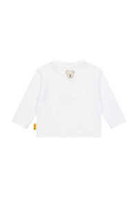 Camicia bianca a maniche lunghe realizzata in un tessuto morbido, con un ricamo a forma di faccia d'orso sulla schiena e un piccolo etichetta gialla di lato.