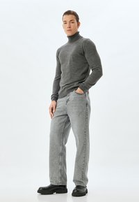 Grå turtlenecktröja, ljusgrå jeans och svarta klumpiga skor med kraftig sula. Avslappnad design med ribbad mudd och lös passform.