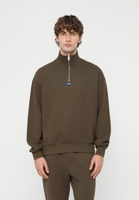 Καφέ φούτερ με ψηλό γιακά, ημίκλειστη με φερμουάρ μπροστά και ριμπ κάτω μέρος. Διαθέτει μπλε λογότυπο "HUGO" στο στήθος. Κατασκευασμένο από μαλακό, υφή υλικό.