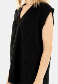 Svart stickad ärmlös topp med V-ringning och vertikal ribbad textur, med en avslappnad passform och mjukt tyg.