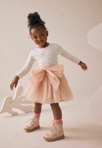 Haut blanc à manches longues avec un motif floral rose, jupe en tulle rose avec un grand nœud, et bottes rose clair avec des chaussettes roses.