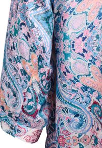 Partie de manche d'un chemisier avec des motifs floraux paisley en bleu, rose et orange sur un tissu léger.