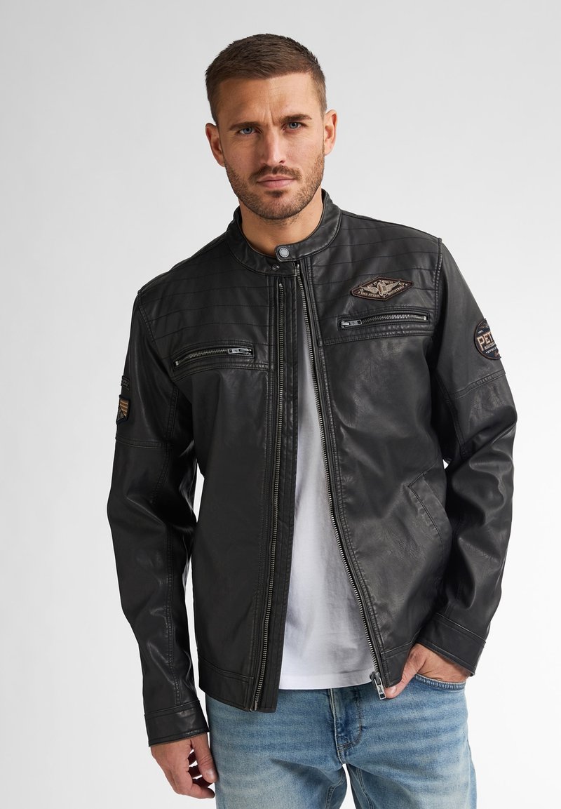 Schwarze Lederjacke mit Stehkragen, mit Reißverschlusstaschen und gestepptem Muster an den Schultern; verfügt über Patches an den Ärmeln.