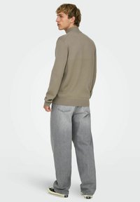 Maglione lavorato a maglia marrone chiaro con collo a mezza zip, abbinato a jeans larghi grigio chiaro e sneaker nere. Tessitura a maglia piatta e vestibilità rilassata.