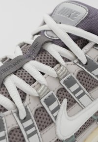 Nike sneakers with a mesh upper in gray and purple, featuring white laces, reflective accents, and a prominent white swoosh logo.