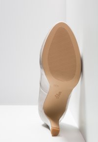 Chaussure à talons hauts en satin avec semelle en caoutchouc beige indiquant la taille 37 et le nom de la marque s.Oliver, photographiée par le dessous sur un fond blanc.