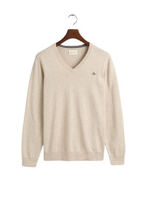 Maglione beige a V realizzato in tessuto morbido, con maniche lunghe e un piccolo logo ricamato sul petto. Orlo e polsini sono a costine.