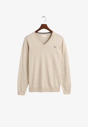 Maglione beige a V realizzato in tessuto morbido, con maniche lunghe e un piccolo logo ricamato sul petto. Orlo e polsini sono a costine.