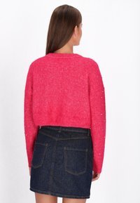 Maglione rosa accorciato con tessuto testurizzato e dettagli di perline sulle maniche, abbinato a una gonna di jeans scura con tasche posteriori.