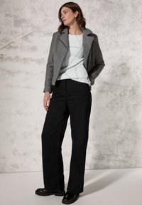 Grijze wolmix jas met revers; lichtblauwe trui met een ruitpatroon; zwarte rechte broek; zwarte chunky schoenen.