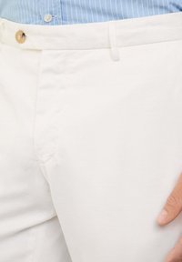 Pantalones de algodón blancos con una textura suave, que presentan un cierre de botón en la parte delantera y bolsillos laterales. La cinturilla es plana y ajustada.
