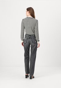 Black and white striped long-sleeve top paired with high-waisted, distressed grey denim jeans, featuring a straight fit and ankle-length.