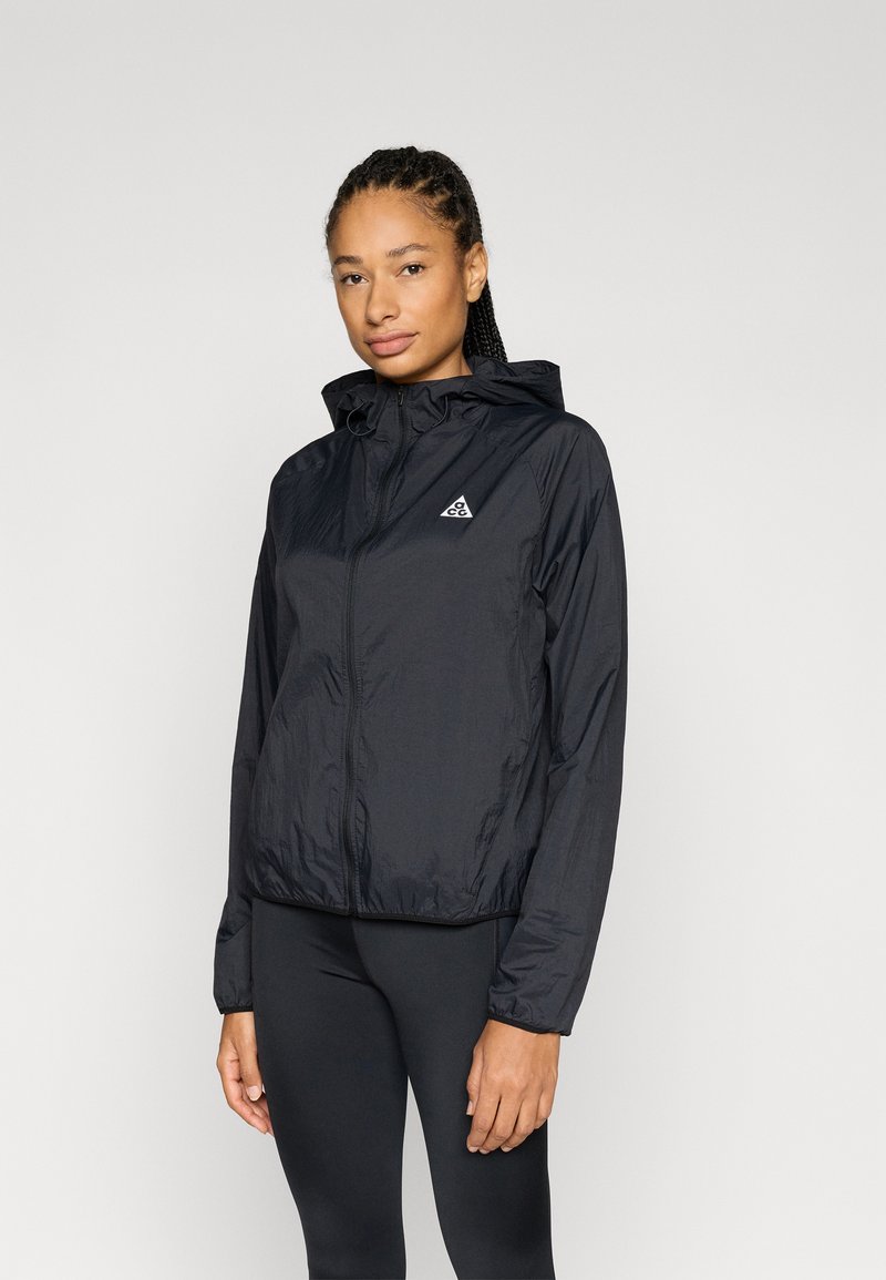 Ελαφρύ μαύρο μπουφάν με φερμουάρ και κουκούλα, με τριγωνικό λογότυπο στο αριστερό στήθος και ελαστικά μανίκια για εφαρμοστή εμφάνιση.