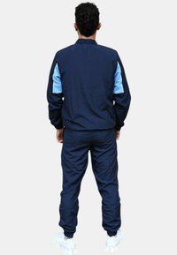 Chándal en azul marino y claro que incluye una chaqueta con cremallera y pantalones a juego, fabricado con una tela suave y con puños y cinturilla elásticos.