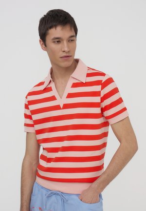 Polo a righe in rosso e rosa, con colletto a V e maniche corte. Materiale morbido, design aderente e bande di colore a contrasto.