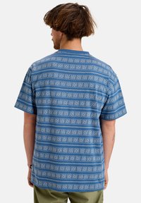 Short-sleeve blue t-shirt featuring a geometric white pattern, made of soft fabric with a relaxed fit and a round neckline.