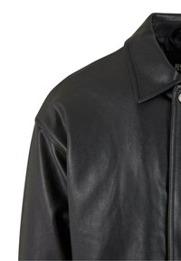 Black leather jacket with a smooth texture, featuring a pointed collar, press studs, and subtle grain pattern on the surface.