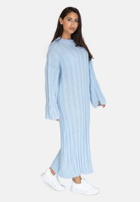 Hellblaue Strickkleid mit vertikaler Rippstruktur, lockerer Passform und langen Ärmeln, getragen mit weißen Turnschuhen.