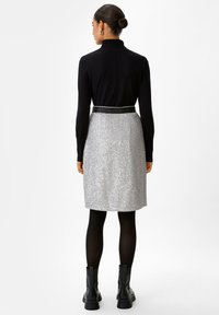 Maglione nero a collo alto abbinato a una gonna a ginocchio di paillettes argentate e stivaletti neri. La gonna presenta una cintura nera.