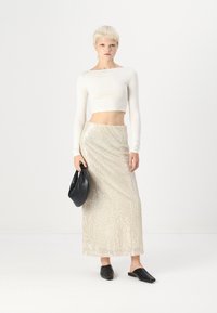 Biely dlhý rukáv crop top v kombinácii so striebornou flitrovou maxi sukňou, doplnený čiernym kabelkov a čiernymi nazúvacími topánkami.