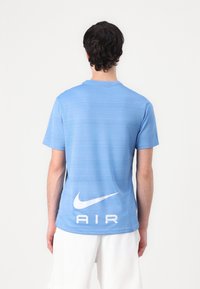 Šviesiai mėlynas sportinis marškinėlis, trumpomis rankovėmis, tekstūruotas audinys, su baltu Nike logotipu ir "AIR" tekstu ant nugaros, apvali iškirptė.
