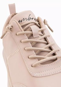 Baskets en cuir beige avec un embout arrondi, des coutures ton sur ton et un design à lacets. Présente un logo en relief sur la languette.