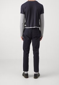 Marinblå kortärmad skjorta över en grå och vit randig långärmad skjorta; ihop med marinblå byxor och svarta skor.